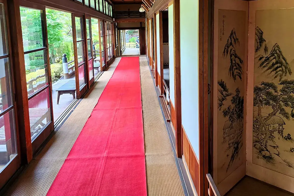 Couloir traditionnel du Yamamoto-tei avec tapis rouge, paravents peints et vue sur le jardin