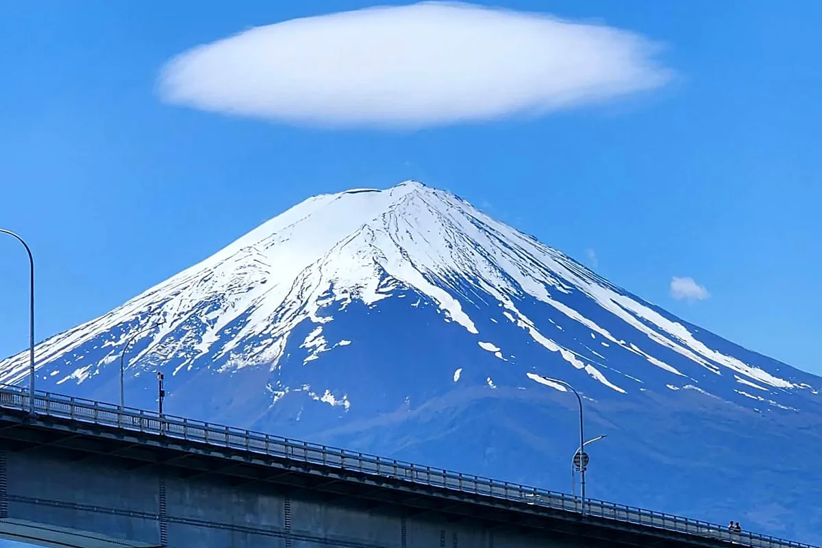 Le mont Fuji enneigé, coiffé d'un nuage lenticulaire, vu depuis un pont