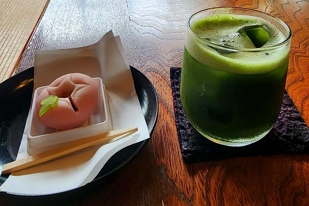 Un wagashi rose et un verre de matcha glacé, posés sur une table en bois